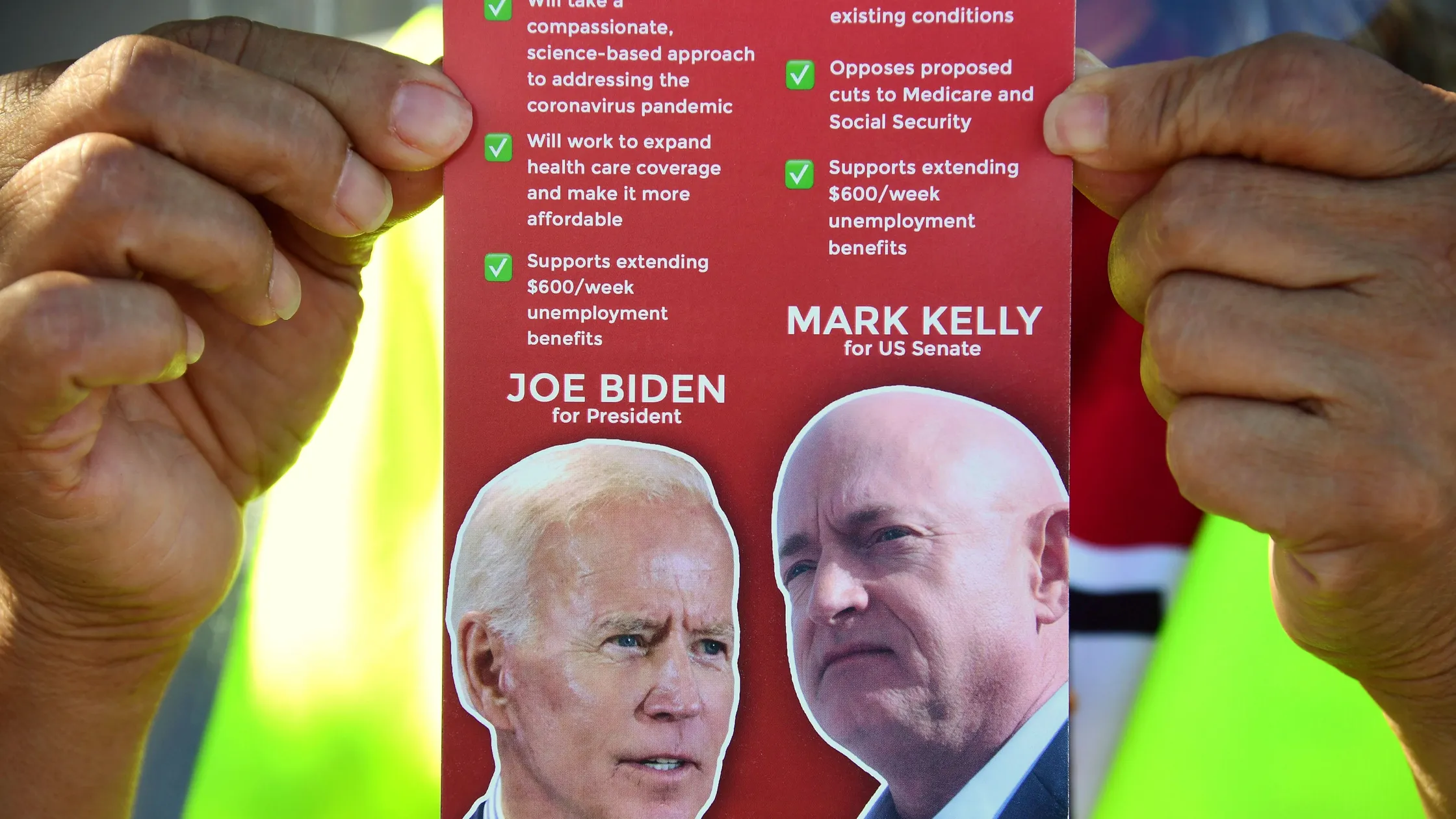A canvasser holds up a campaign flyer featuring Joe Biden for President and Mark Kelly for U.S. Senate, listing their positions on healthcare, unemployment benefits, and Medicare during the 2020 Arizona election campaign.